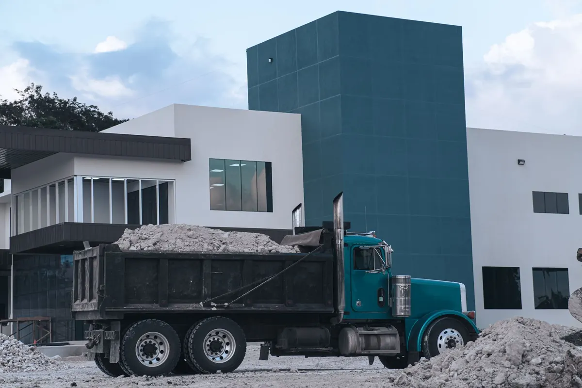 Long-nose dump truck loaded with rubble parked in front of a modern commercial building